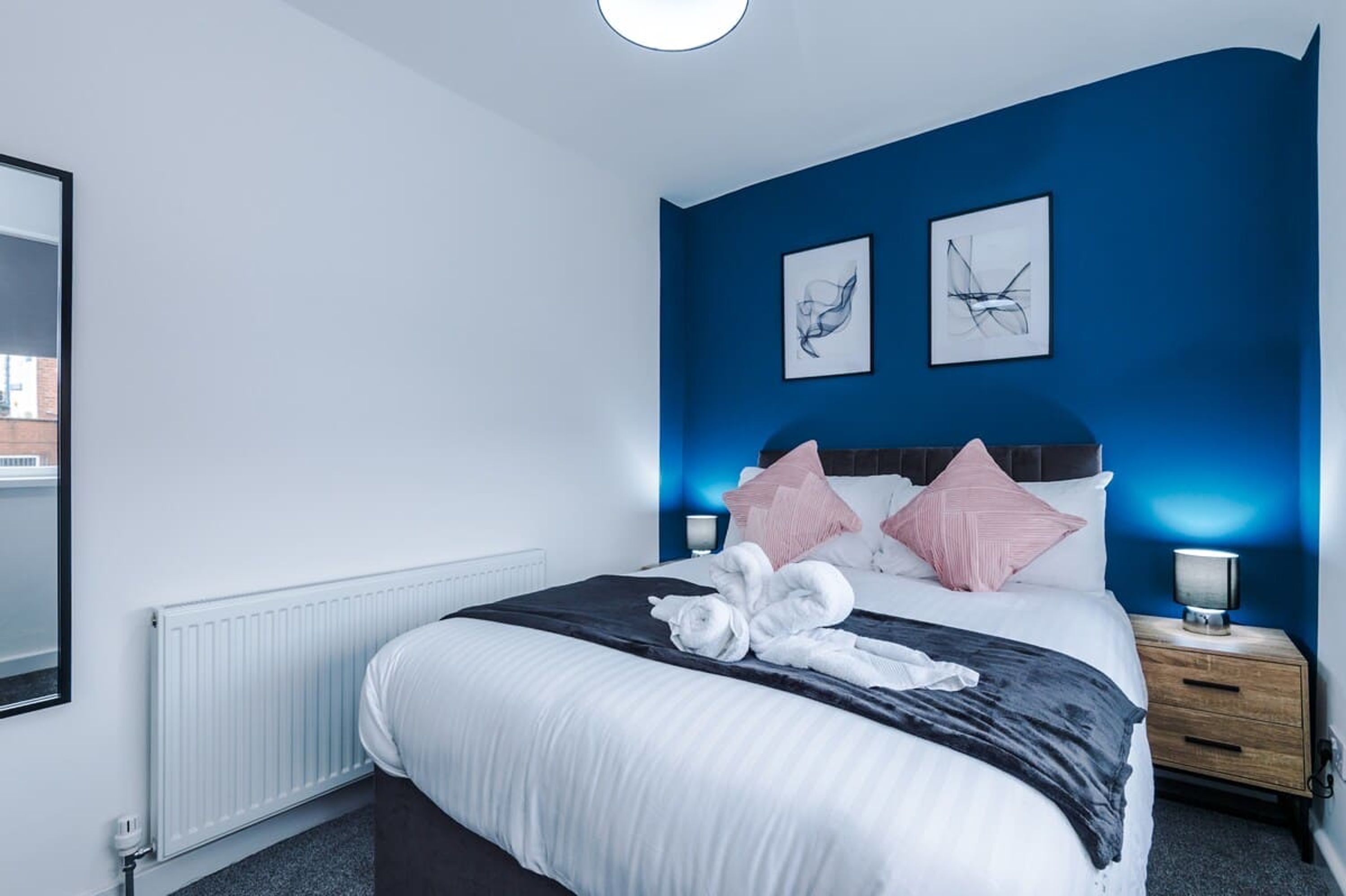 A hotel room with a large bed, a nightstand, two wall-mounted artworks, and a window with a view.