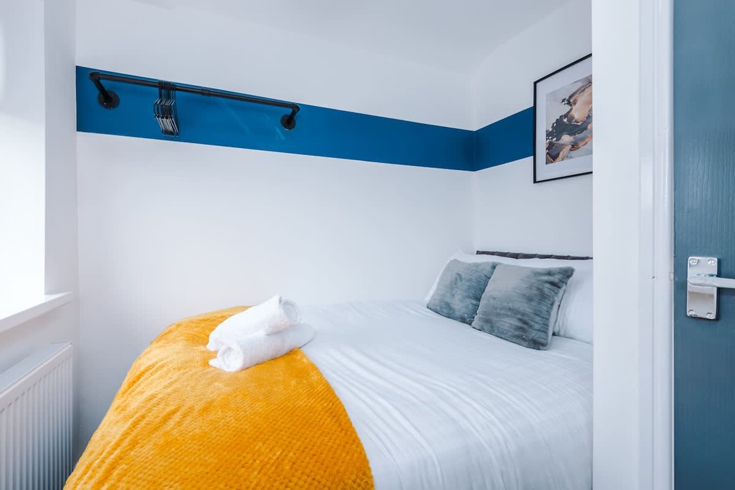 A hotel room with a bed, a blue accent wall, a framed picture, and a towel on the bed.