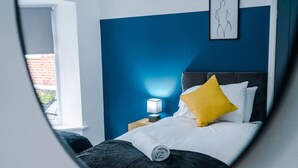 A hotel room with a bed, a nightstand, a lamp, and a framed artwork on the wall. - Spacious 3-bed Ideal for Long-term Business (Manchester)