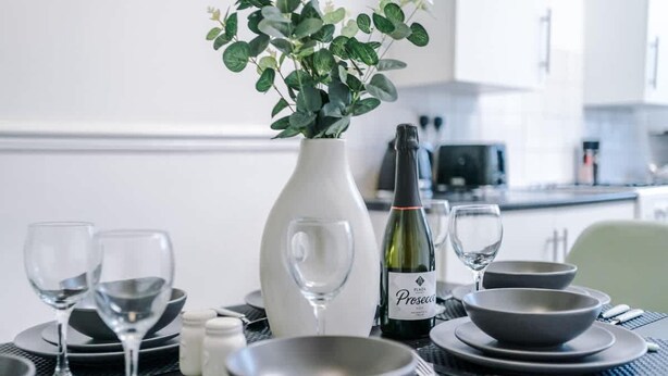 A dining table set with plates, bowls, wine glasses, and a bottle of Prosecco. - Spacious Home Ideal for Contractors Sleeps 7 (Manchester)