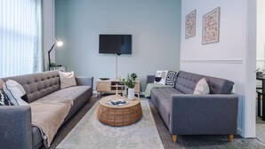 A living room with two sofas, a round coffee table, a flat-screen TV, and a window with blinds. - Spacious Home Ideal for Contractors Sleeps 7 (Manchester)