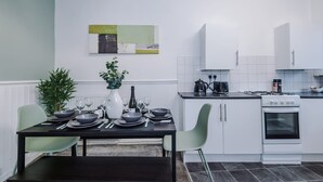 A modern kitchen with white cabinets, a dining table set for four, and a small dining area. - Spacious Home Ideal for Contractors Sleeps 7 (Manchester)