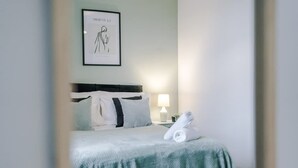 A neatly made bed with a green bedspread, a pillow with a black stripe, and a rolled towel on the side. - Spacious Home Ideal for Contractors Sleeps 7 (Manchester)
