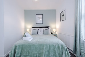 A neatly made bed with a green bedspread, two bedside lamps, and two framed pictures on the wall. - Spacious Home Ideal for Contractors Sleeps 7 (Manchester)