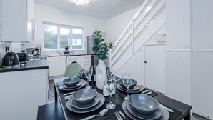 A modern kitchen with white cabinets, a dining area with a black table set for four, and a staircase leading to another level. - Spacious Home Ideal for Contractors Sleeps 7 (Manchester)