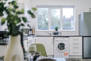 A modern kitchen with a washing machine, a refrigerator, and a window with a view of trees. - Spacious Home Ideal for Contractors Sleeps 7 (Manchester)