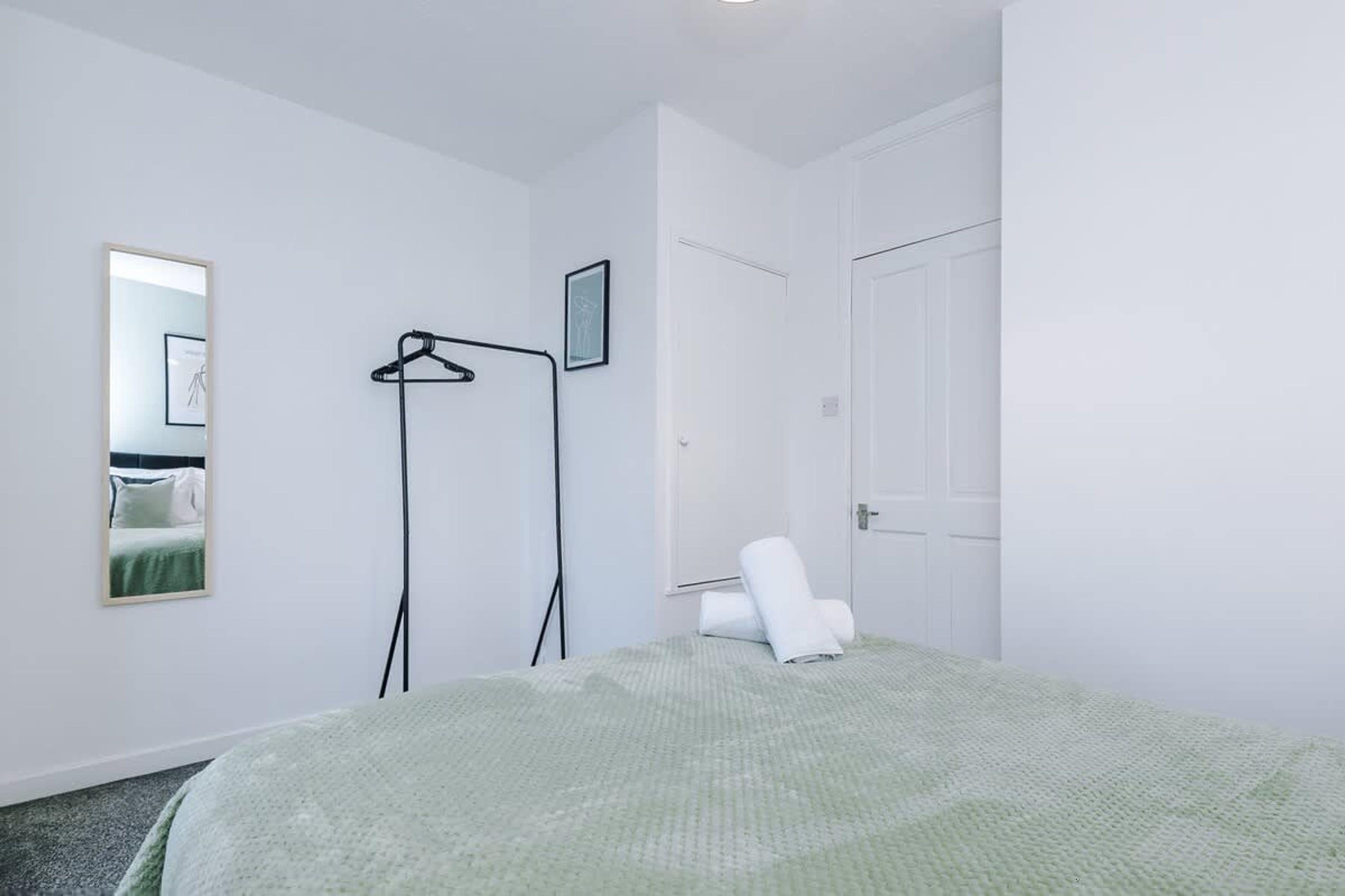 Ein Schlafzimmer mit einem Bett, einem Kleiderständer, einer Tür und einem gerahmten Bild an der Wand.