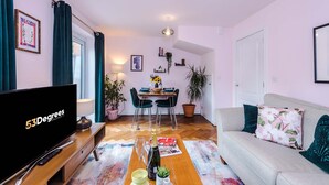 Una sala de estar con una televisión de pantalla plana, una mesa de comedor con sillas, un sofá y una mesa baja.