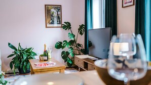 Una habitación con una mesa de madera, una planta en maceta, un televisor y una copa de vino.