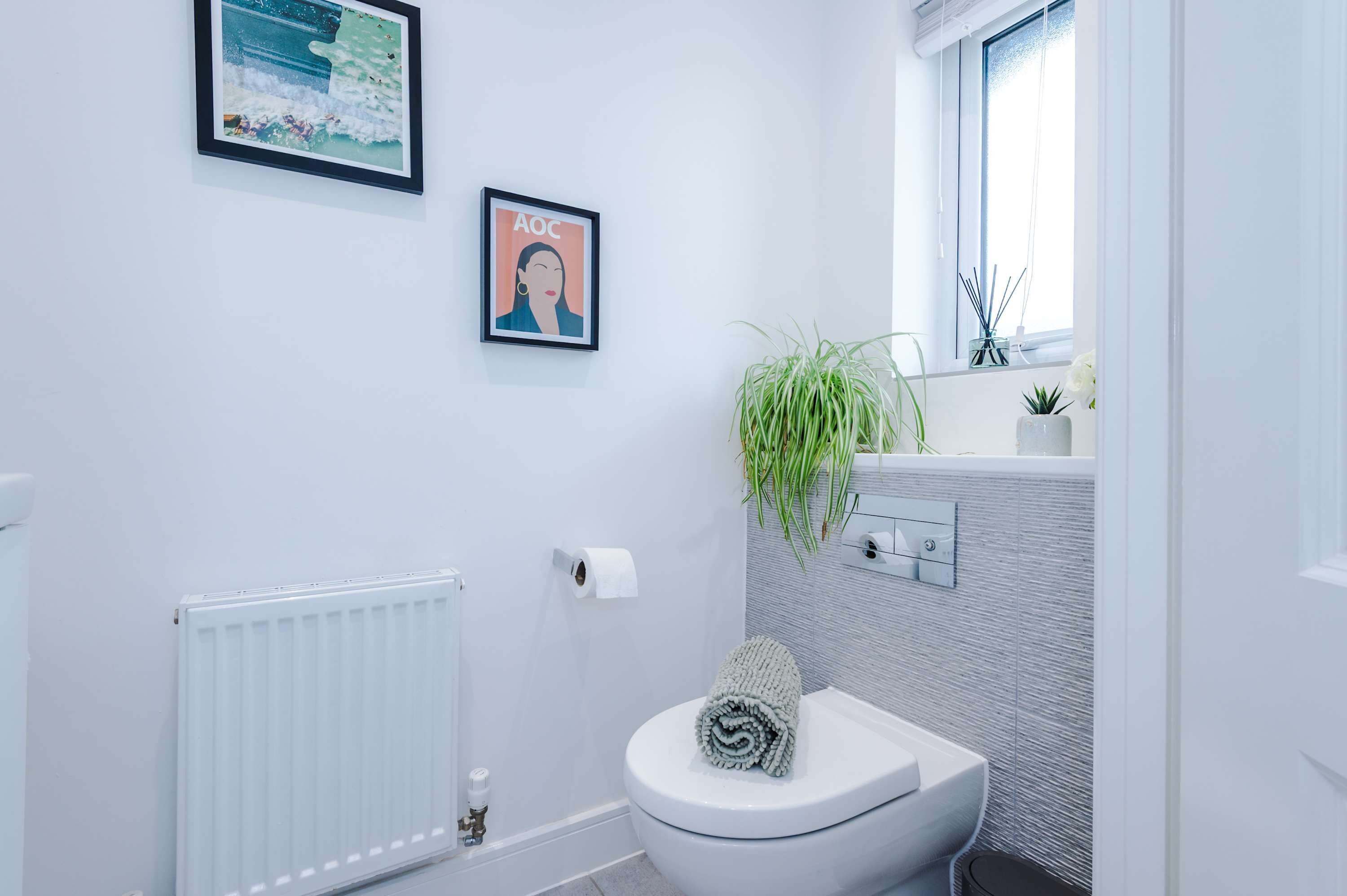 Ein modernes Badezimmer mit Toilette, Handtuchwärmer, einem gerahmten Bild und einem Blumentopf.