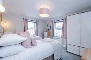 A bedroom with two beds, a wardrobe, a mirror, and a window with curtains. - Modern City Centre 3 Bed Apartment Great for Couples (Chester)
