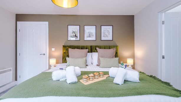 A neatly arranged bedroom with a bed, pillows, a bedside table, a lamp, and a green rug. - Modern City Centre 3 Bed Apartment Great for Couples (Chester)