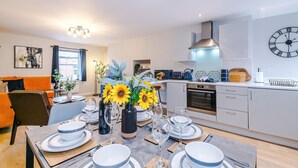 A modern kitchen with white cabinets, a built-in oven, and a clock on the wall. - Modern City Centre 3 Bed Apartment Great for Couples (Chester)