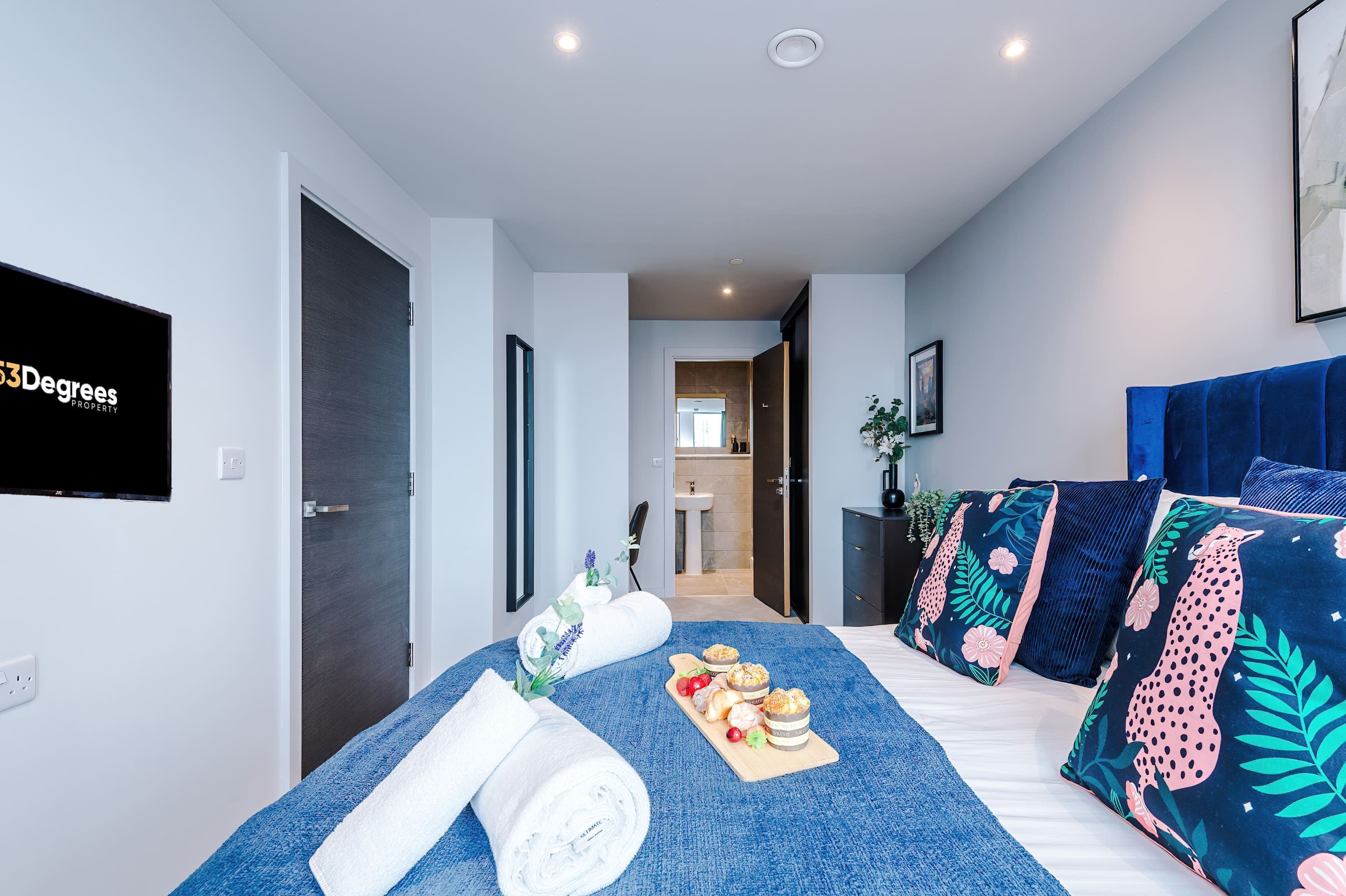Ein modernes Hotelzimmer mit Bett, Flachbildfernseher und Blick ins Bad.
