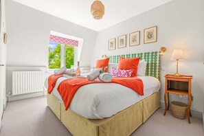 A bedroom with a bed, a window, a lamp, and a wall with framed pictures. - Chic 2BR Duplex Home W London With Private Patio (London)
