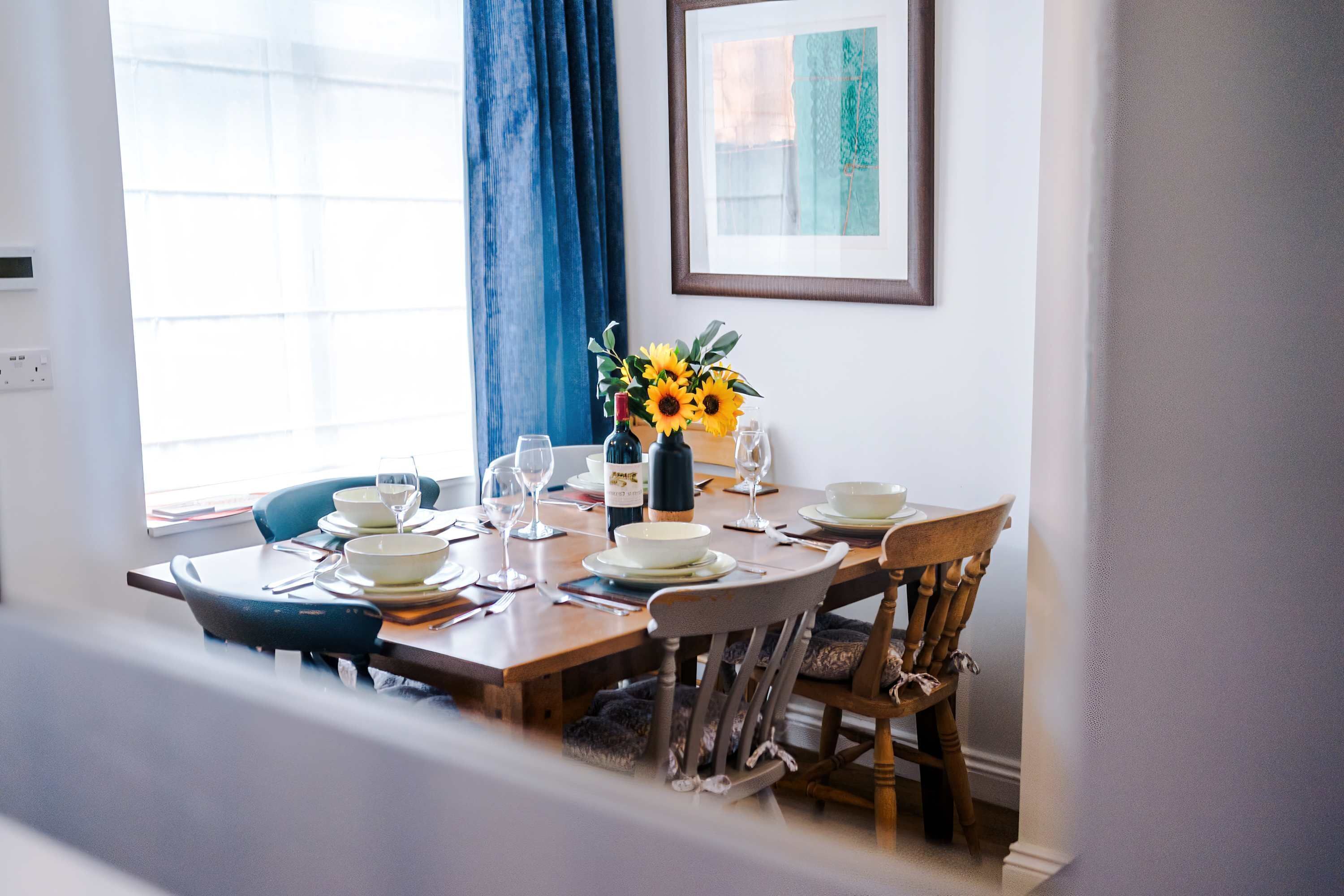 Een eettafel gedekt met borden, glazen en een vaas met zonnebloemen.
