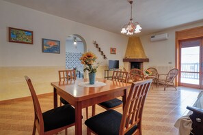 Un comedor con mesa de madera, sillas, un jarrón con flores, televisor y chimenea.