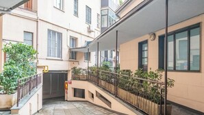 Ein schmaler Stadtgang mit einer gebogenen Treppe, Metallgeländern und Blumentöpfen.