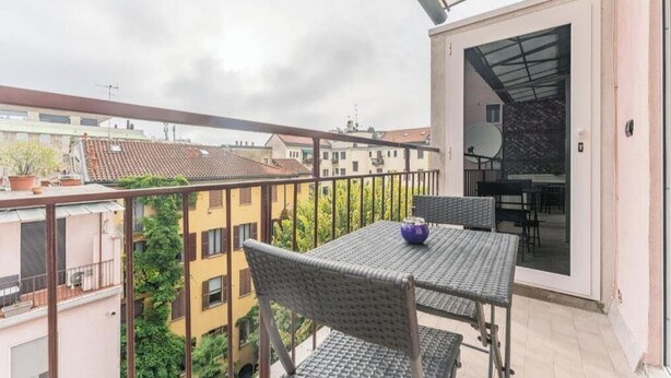 Ein Balkon mit Tisch und Stühlen, Blick auf benachbarte Gebäude und eine Tür zu einem Innenbereich.