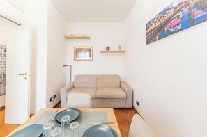 A living room with a beige sofa, a dining table with plates and glasses, and a painting on the wall. - AP1 - Elegant and Cozy Apartment in the Heart of Milan (Milano)