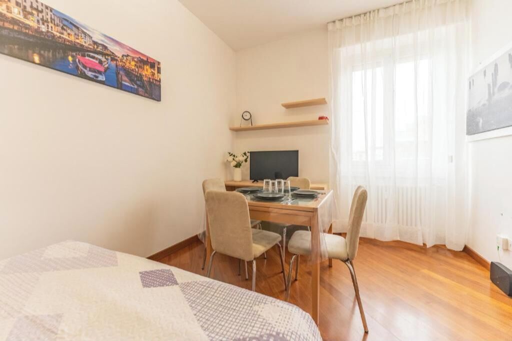 Une chambre d’hôtel comprenant un lit, une table à manger avec des chaises, une télévision et une fenêtre avec des rideaux.