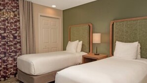 Une chambre d’hôtel avec deux lits, une porte, un miroir et une table de chevet avec une lampe.