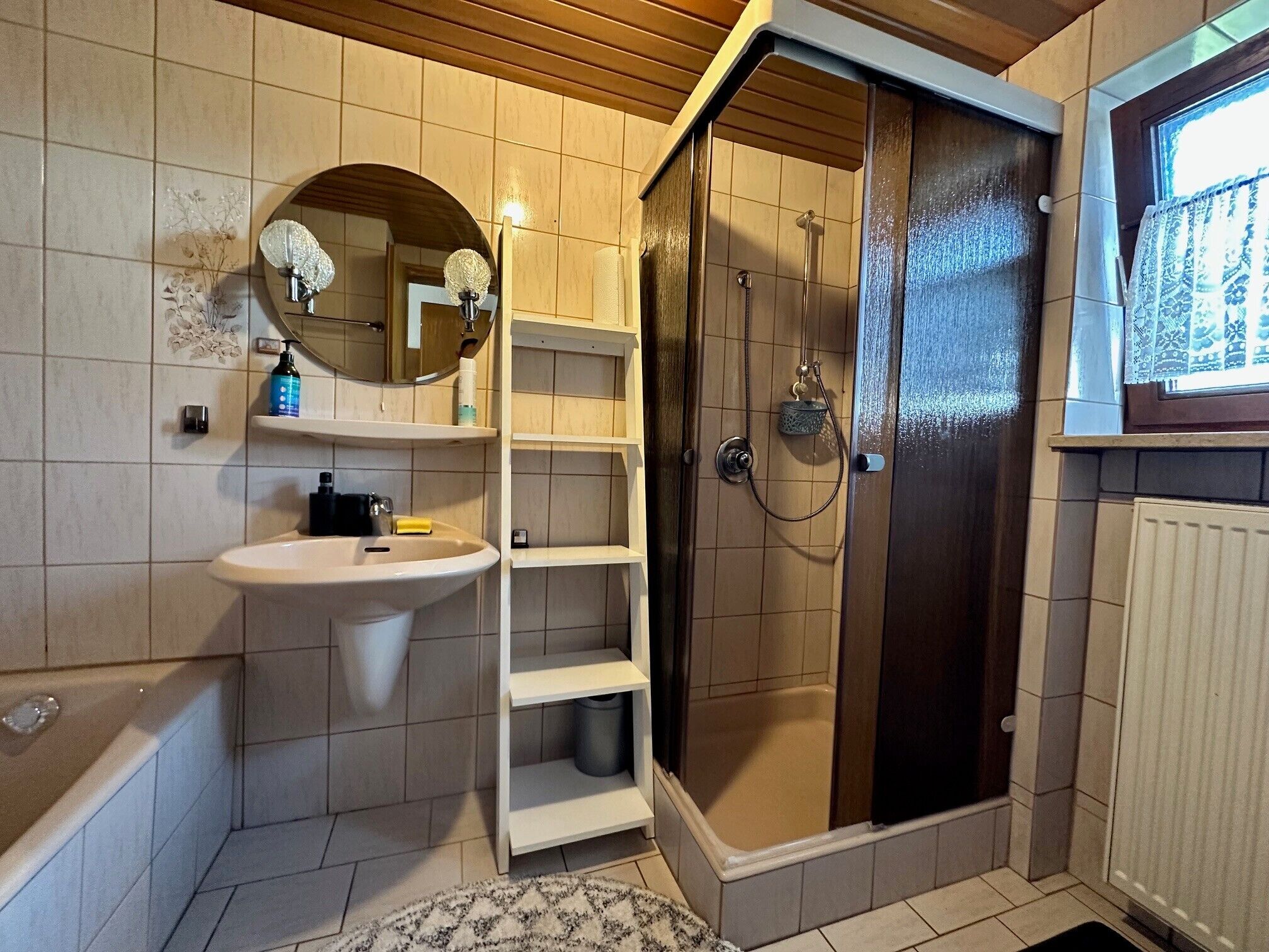 Un baño con lavabo, espejo, estantes, ducha y ventana.
