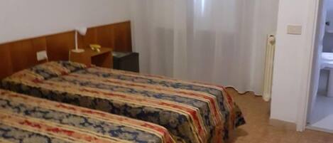 A room with two beds, a wooden headboard, a small table, and a window with curtains.