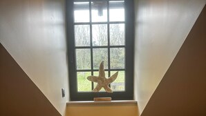 Une pièce avec un plafond en pente, une fenêtre décorée d’une étoile de mer et un tableau encadré posé sur le sol.