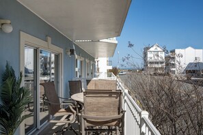 A balcony with wicker chairs and a table, overlooking a parking lot and buildings. - Luxury 4-bedroom oceanblock retreat on 138th Street offering plenty of space and a pool (Ocean City)