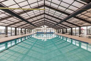 Una gran piscina interior con techo alto y paneles de vidrio, rodeada de sillas y vistas al exterior.