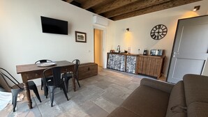 Ein Wohnzimmer mit Holzboden, ein Essbereich mit Tisch und Stühlen, eine Küchenzeile mit Spüle und Schränken sowie eine Uhr an der Wand.