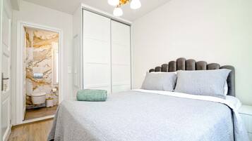 Un dormitorio con cama, armario y baño a la vista, tras una puerta abierta.
