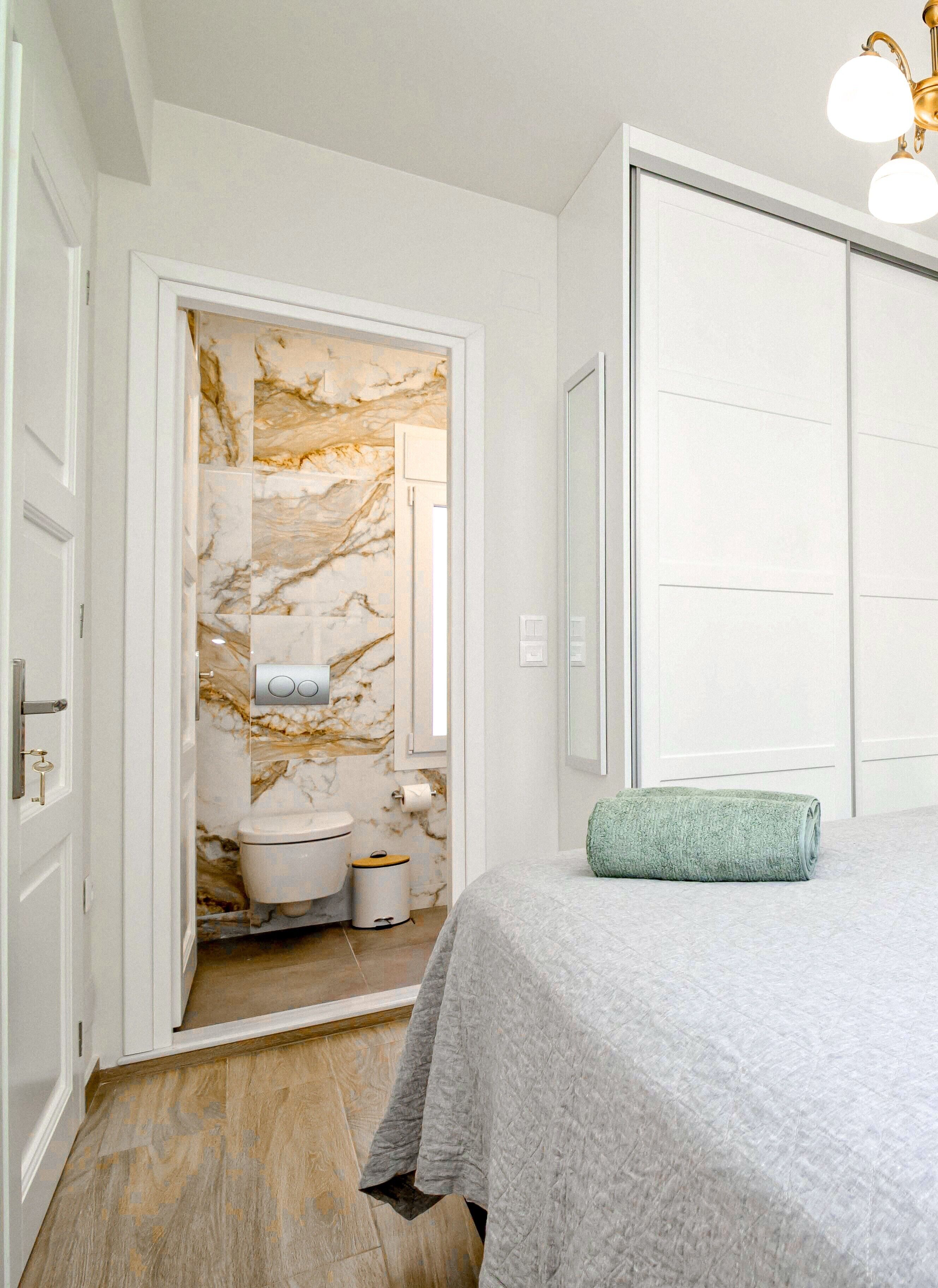 Un dormitorio con cama, un baño con inodoro y lavabo, y una pared de mármol.