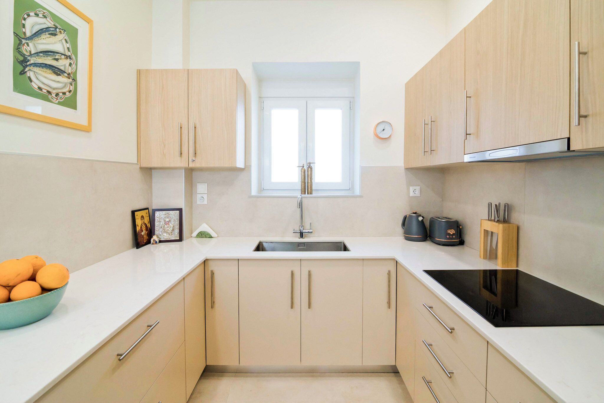 A modern kitchen with light wood cabinets, a black stovetop, and a window above the sink.