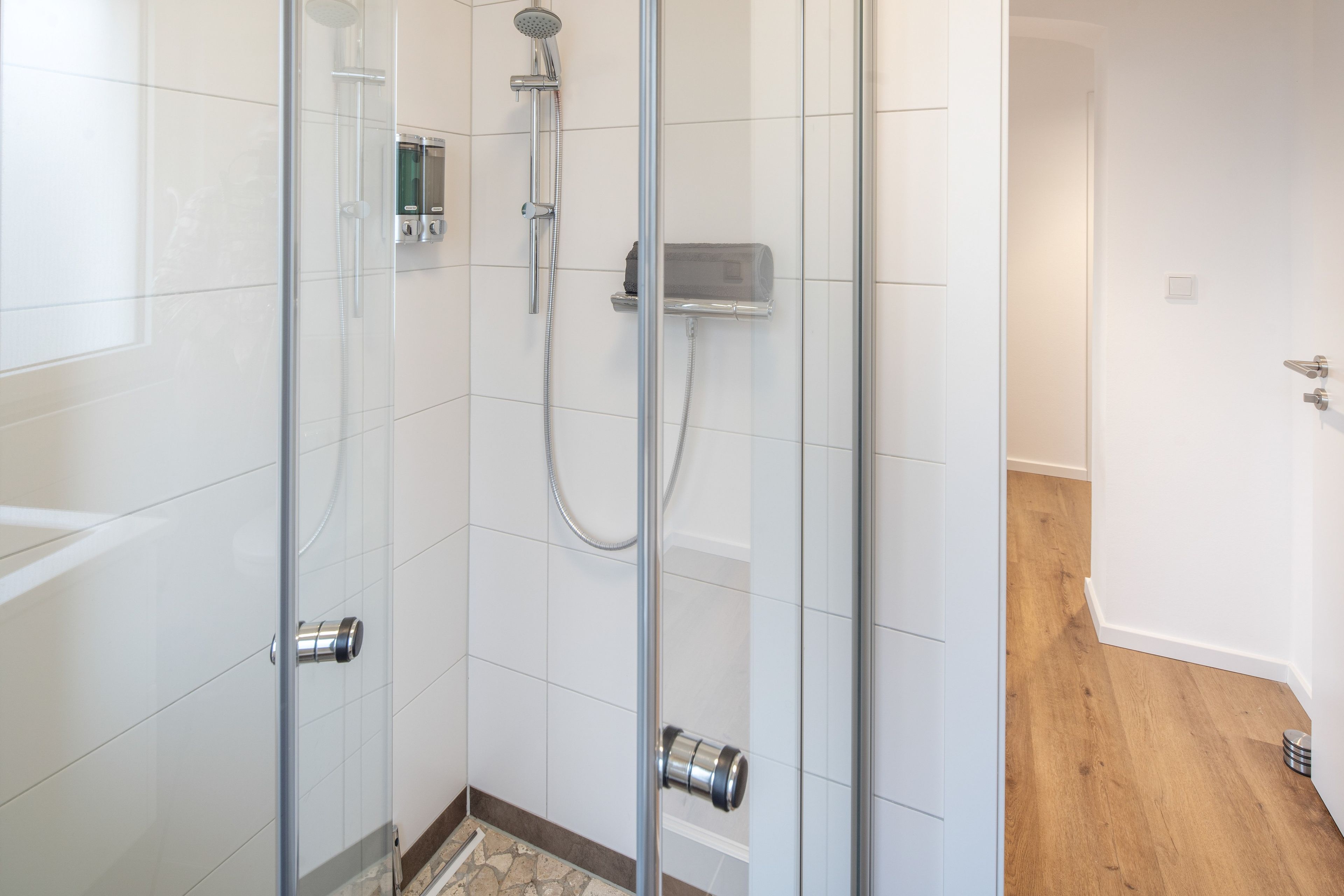 Ein modernes Badezimmer mit einer gläsernen Dusche, einer Handbrause und einem an der Wand montierten Bedienfeld.