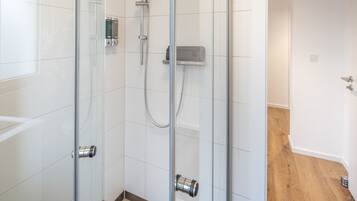 Ein modernes Badezimmer mit einer gläsernen Dusche, einer Handbrause und einem an der Wand montierten Bedienfeld.