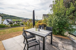 Eine Terrasse im Freien mit Tisch, Stühlen, einer Weinflasche und einem Weinglas.