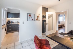 Een moderne keuken met donkere kastjes, een koffieapparaat en een eethoek met een rode stoel en een tafel.