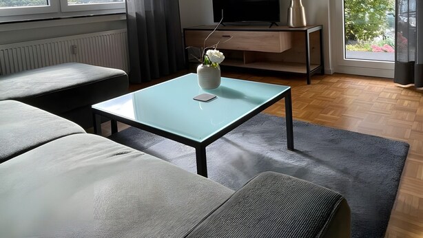 Una sala de estar moderna con sofá, mesa de centro, televisor y un amplio ventanal con vistas al exterior.