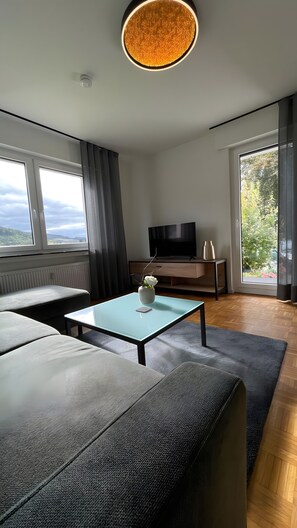 Un salon moderne comprenant un canapé, une table basse, un téléviseur et une grande fenêtre donnant sur l’extérieur.