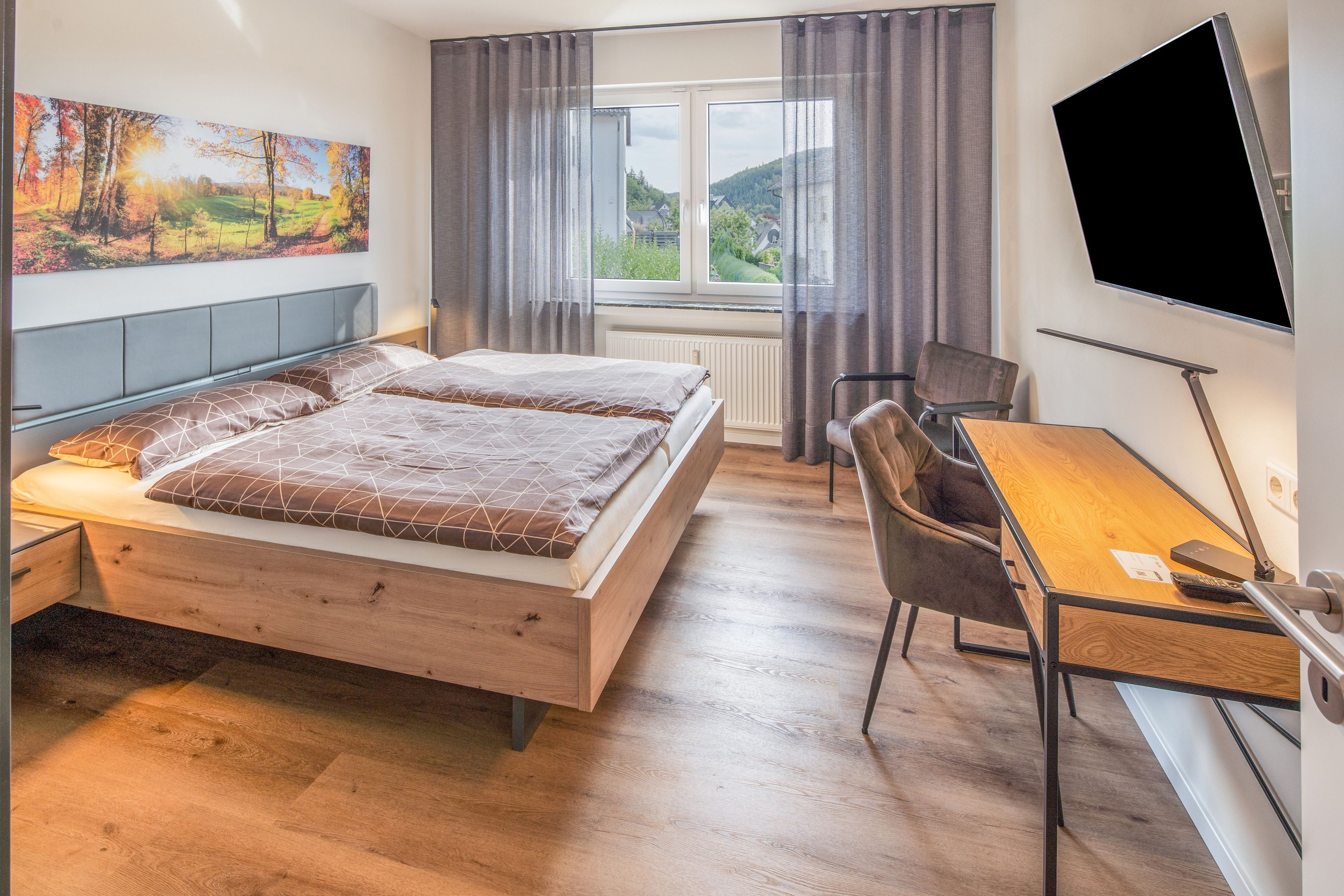 A bedroom with a bed, a desk, a chair, a TV, and a window with curtains.