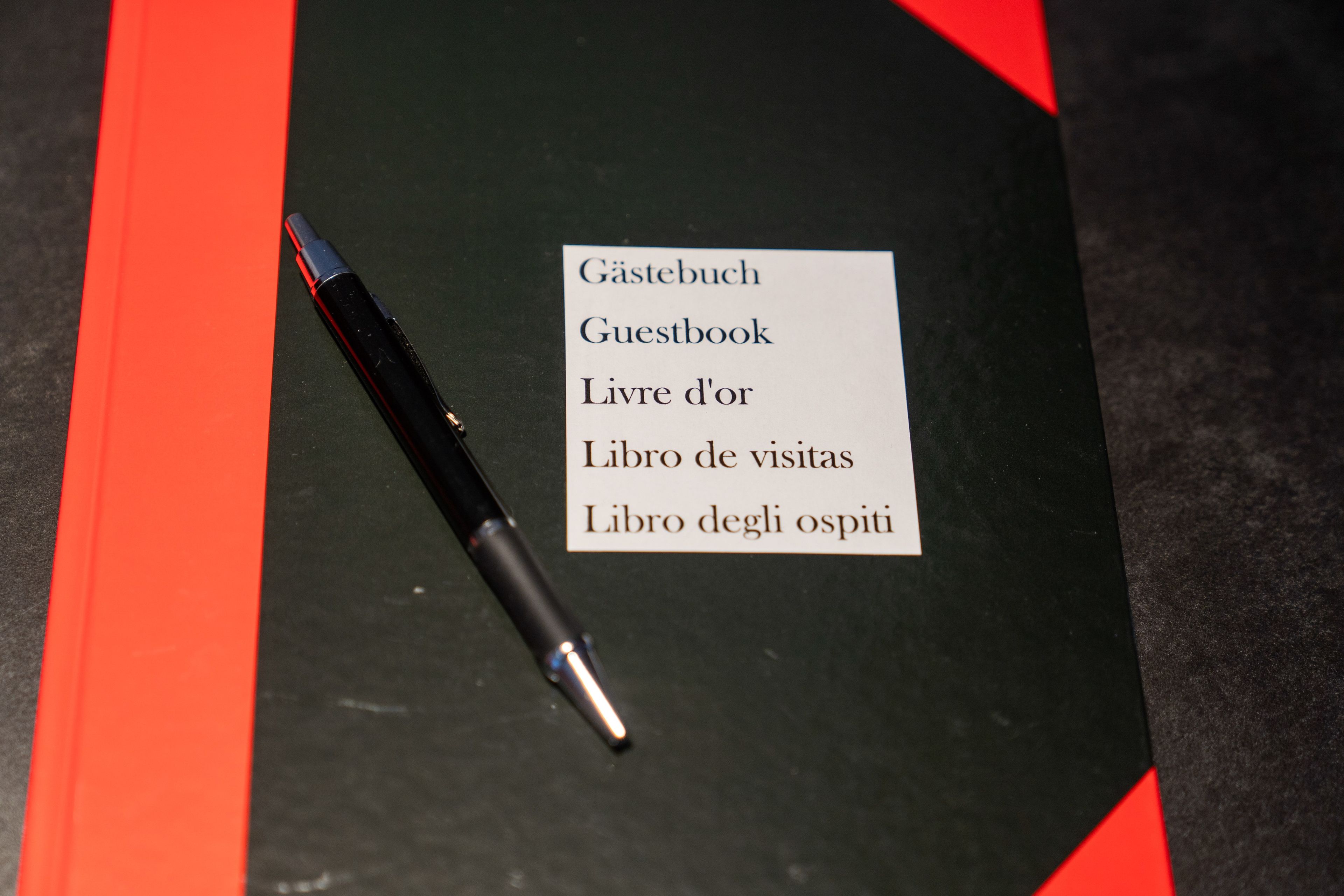 Ein schwarzes Notizbuch mit einem Stift darauf, beschriftet als Gästebuch.