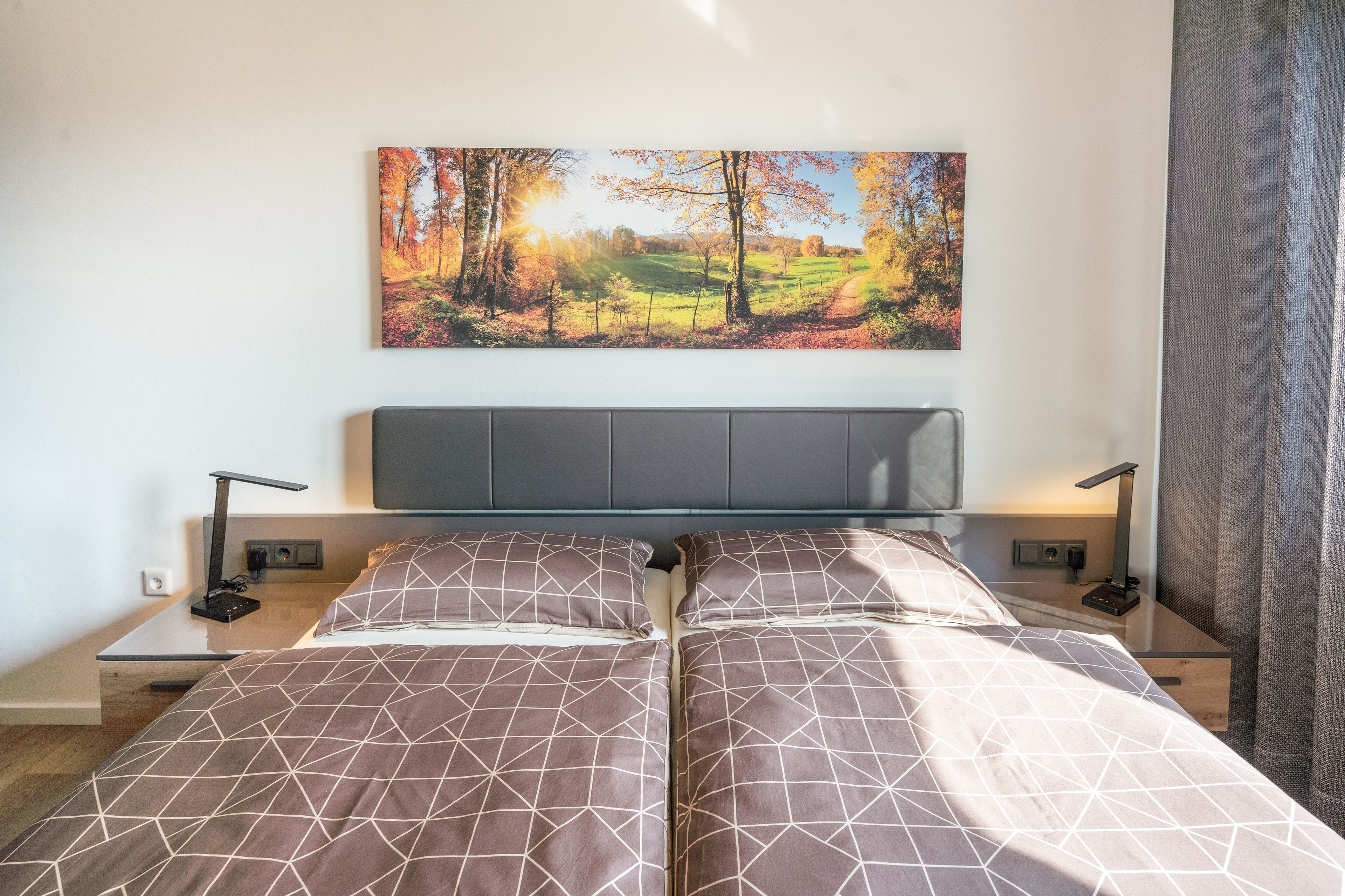 Ein Schlafzimmer mit einem Bett, zwei Nachttischen, einem an der Wand montierten Fernseher und einem Waldgemälde.