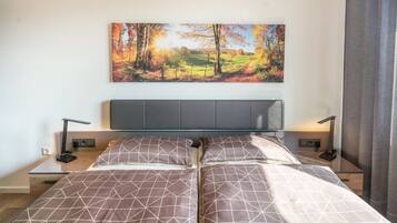 Ein Schlafzimmer mit einem Bett, zwei Nachttischen, einem an der Wand montierten Fernseher und einem Waldgemälde.