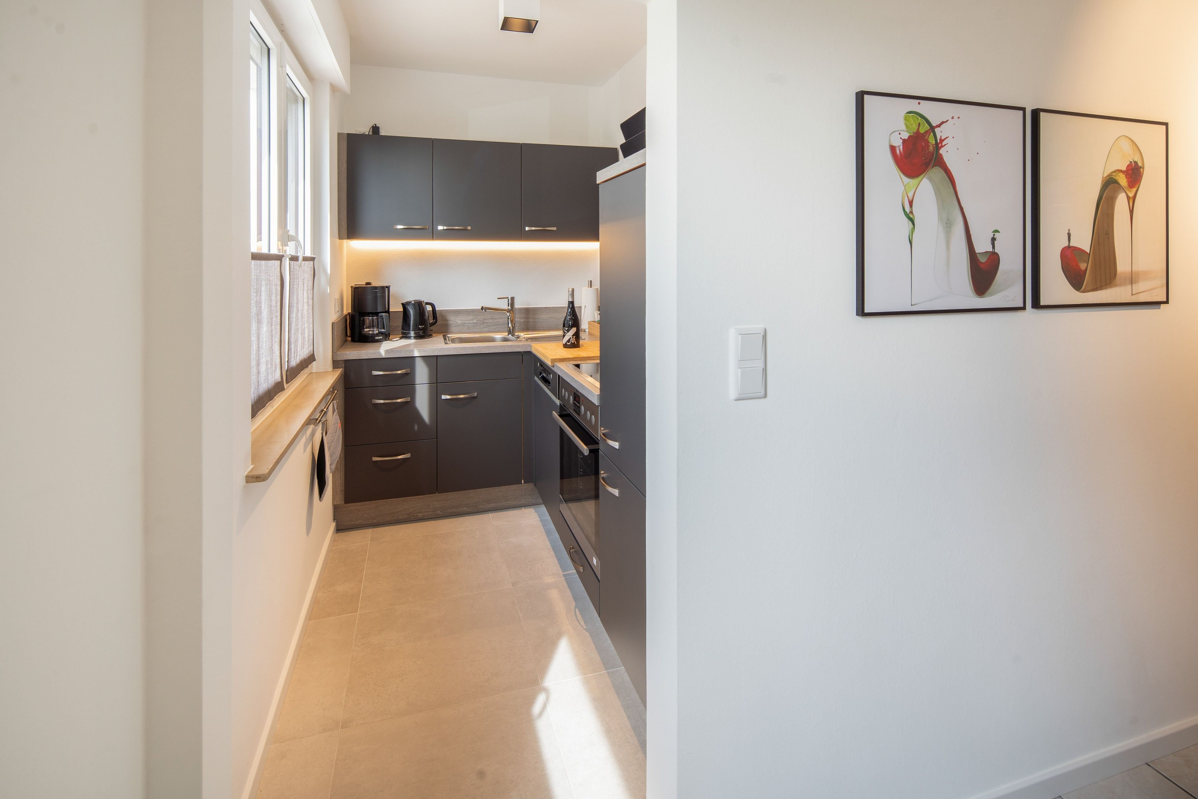 A modern kitchen with dark cabinetry, a coffee maker, and a wine bottle on the counter.
