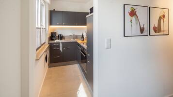 A modern kitchen with dark cabinetry, a coffee maker, and a wine bottle on the counter.