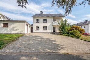 Een twee verdiepingen tellend huis met een geplaveid opritje naar de ingang.