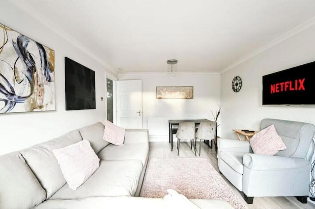 A modern living room with a sofa, armchair, and a flat-screen TV mounted on the wall.