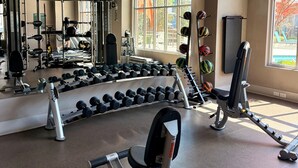 Une salle de sport équipée de matériel d’exercice, de miroirs et de grandes fenêtres.
